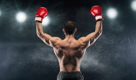 boxer champion enjoying his victory on lights and standing back to the camera, black studio background