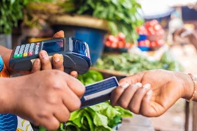 close up og someone giving a woman holding a pos her credit card in a local market