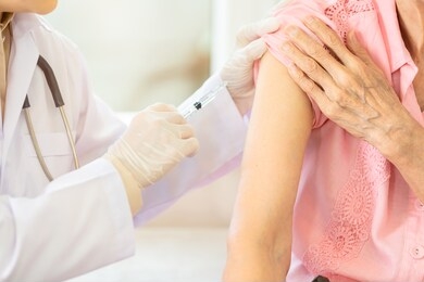 closeup,asian female doctor with syringe doing injection vaccine,flu,influenza in the shoulder of senior woman,young nurse injecting,vaccinating elderly patient,vaccination,medicine,healthcare concept
