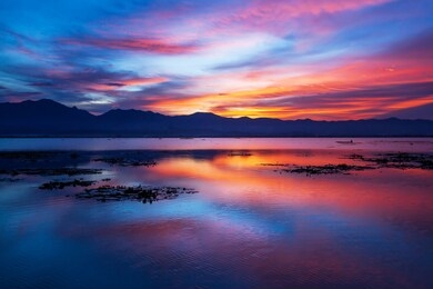 dramatic clouds and sunset sky over the lake and mountain range in backgrounds, colourful clouds reflecting on surface of water, fisherman on fishing boat in the lake. phayao lake, thailand.