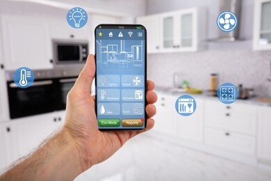 close-up of man's hand holding mobile with smart home control icon feature with kitchen background