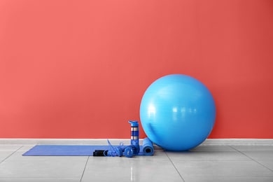 set of sports equipment with fitness ball and bottle of water near color wall