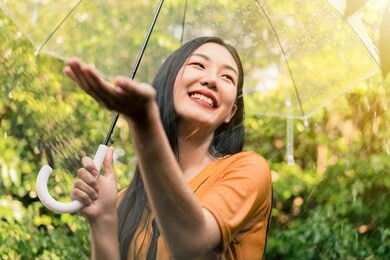 young asian woman smiling and enjoying under umbrella in the rain, green nature background, rainy season.