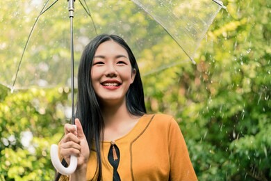 young asian woman smiling with happiness under umbrella in the rain, rainy season.