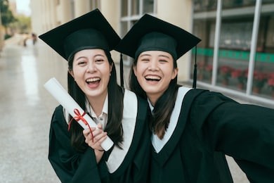 selfie for memories. group cheerful asian female graduates posing make self photo showing diploma scroll cheerful laughing. attractive lady students taking picture wear gowns and mortar board in hall