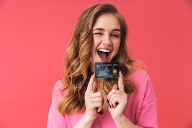beautiful young casual blonde girl standing isolated over pink background, showing plastic credit card