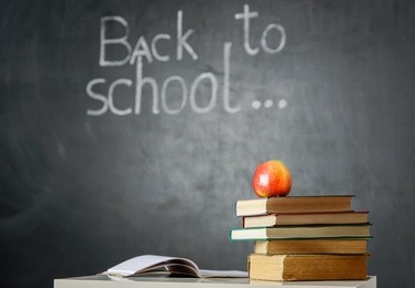 still life with school books and apple against blackboard with "back to school" on background
