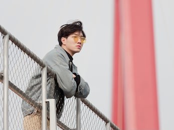 portrait of a handsome chinese young man standing on bridge and looking away in wind, has nothing to do just waiting.