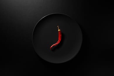one dry red hot chili pepper served in black plate on black background. top view 