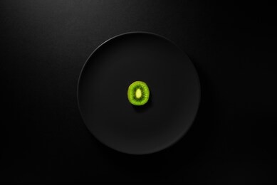 one kiwi slice served in black plate on moody black background. top view. healthy diet concept