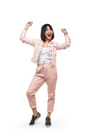 full body excited asian female in stylish outfit smiling and looking away while dancing against white background