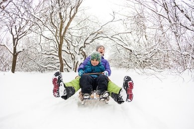mother with a child riding on a sled. a woman with her son rides down the hill in a sleigh and screaming. the boy spends time with his parent. funny winter holidays.