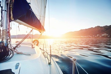 sailing yacht boat on on ocean water at sunrise with flare and outdoor lifestyle