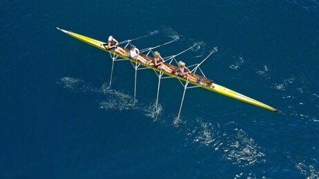 aerial drone bird's eye view of yellow sport canoe operated by team of young women in deep blue sea waters
