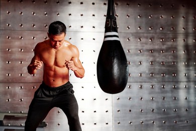 shirtless muscular boxer warming up with punching bag before fight in gym
