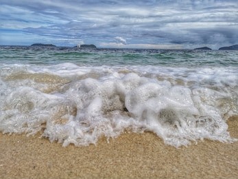 closeup with the sandy beach splashing water and swash wave in kota kinabalu, tanjung aru beach. sabah, malaysia.