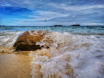 closeup with the beautiful splashing swash silky smooth water over a single rock in tangjung aru beach, kota kinabalu, sabah. malaysia, borneo.