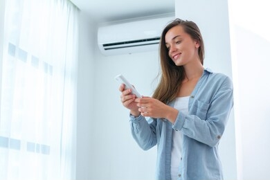 portrait of young attractive woman adjusts air conditioner temperature using remote control in room at home. 