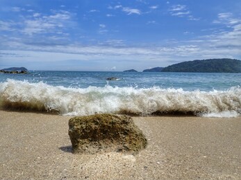 closeup with the splashing swash water over a single rock on the beach of kota kinabalu, sabah. malaysia, borneo.