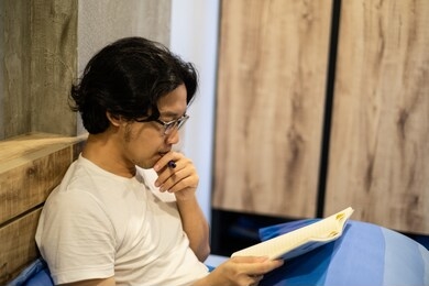 asian handsome man reading a book on the bed