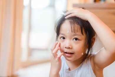 little asian girl applying protective sunscreen on face at home for ready to go to the beach.kid girl hand putting sun lotion on her face.