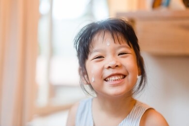 little asian girl applying protective sunscreen on face at home for ready to go to the beach.kid girl hand putting sun lotion on her face.