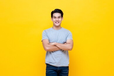 casual young handsome man smiling and looking at camera with arms crossed isolated over yellow background