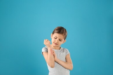 little girl scratching forearm on color background. allergy symptoms