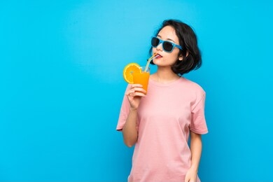 asian young woman over isolated blue background holding a cocktail