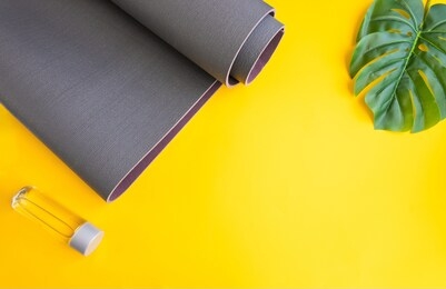 close up of grey exercise mat and water bottle on yellow background with palm leaf. concept for practice yoga, pilates or any  physical workout  at summer.