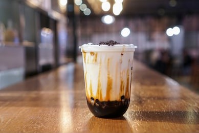 brown sugar bubble drink. a plastic cup of fresh milk and brown sugar boba/bubble toppings and topped with chocolate cookies on wooden table.