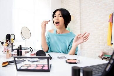 young asian woman beauty vlogger about to applying lipstick on her lips doing makeup tutorial broadcasting online