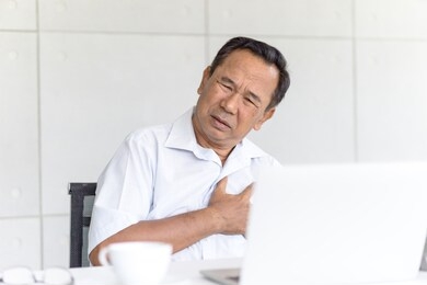 senior man having paint at heart while sitting in front of computer. asian middle aged guy with heart attack.
