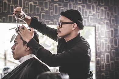 portrait of professional barber making hair cut of his attractive man costumer with scissors and comb in vintage barbershop
