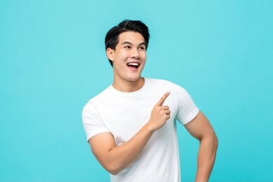 handsome healthy young asian man smiling with his finger pointing isolated on light blue studio background