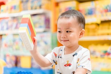 2.5 years old little asian toddler boy playing colorful toy block in department store kid club.motor skill and executive functions concept.