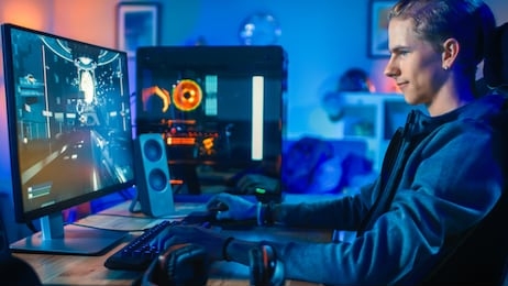 cheerful gamer playing first-person shooter online video game on his powerful personal computer. room and pc have colorful neon led lights. cozy evening at home.