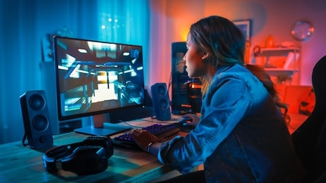 pretty and excited black gamer girl has a tense moment in her first-person online shooter video game on her computer. room and pc have colorful neon led lights. cozy evening at home.