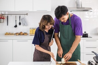 smiling  happy young asian couple wearing apron and cooking together in a white kitchen background