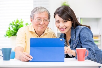 young daughter teach elder father use tablet pc at home