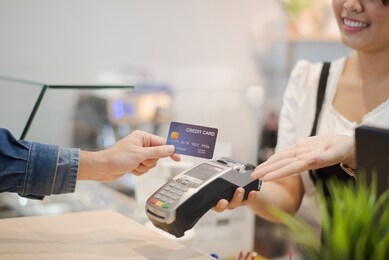 hand of man customer using wireless or contactless payment of a credit card. young asian cashier or seller are smiling to accept payment by nfc technology at retail shop. contactless payment concept.