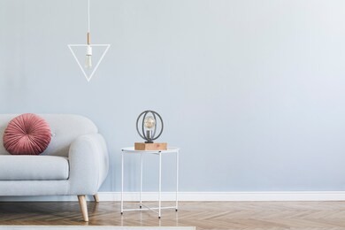 minimalistic and stylish interior of open space with design gray sofa, coffee table, lamps, pillow. gray background walls, brown wooden parquet. modern concept of room. template. copy space.