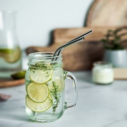 cold drink in mason jar with metal straws on kitchen table. lemonade or detox water with lime and thyme in glass jar wit metal straw indoor. recyclable straws, zero waste concept