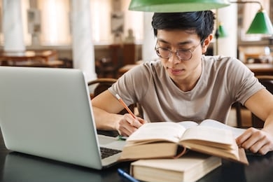 smiling asian teenager student studying at the library