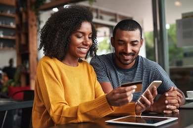 man looking at his girlfriend shopping online in cafe