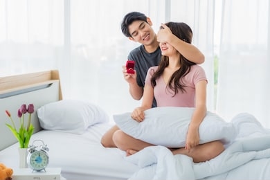 handsome young man closed his eyes girlfriend proposing to excited surprised by wedding ring in mornig on bed with happiness in bedroom. wedding and romantic surprise concept.