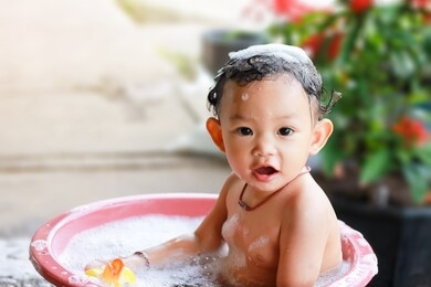 happy baby asian girl take a bath with bubbles soap and playing a duck toy. she sitting in a bathtub.