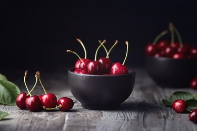 ripe red cherries in a bowl and next to it on wooden table.