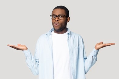 doubtful african american millennial male in glasses isolated on grey studio background compare offers or prices, unsure black man keep hands aside doubt over deal, make decision or choice