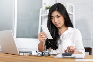 the panic asian woman checking expensive electricity and house hold bills, reads documents attentively, prepares financial report, calculates on laptop computer. finance interior,domestic housework 